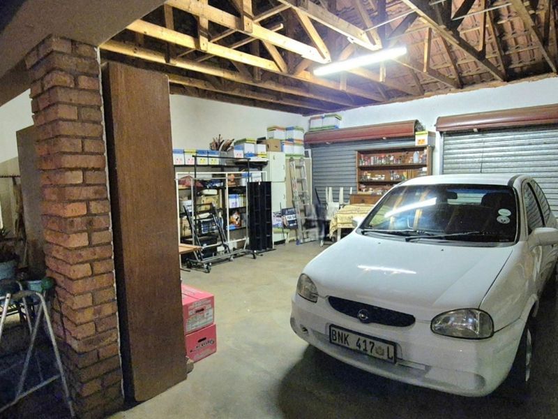 Spacious garage featuring exposed timber roof trusses, concrete flooring, and two secure roller shutter doors.