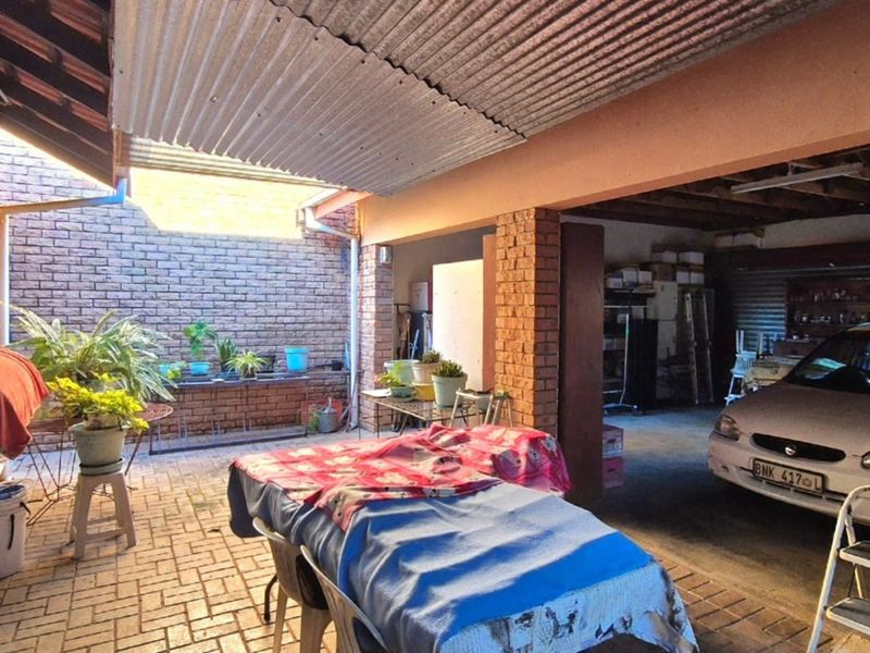 A covered outdoor patio area featuring exposed brick walls, paved flooring, and a corrugated iron roof, providing a functional space for outdoor activities.