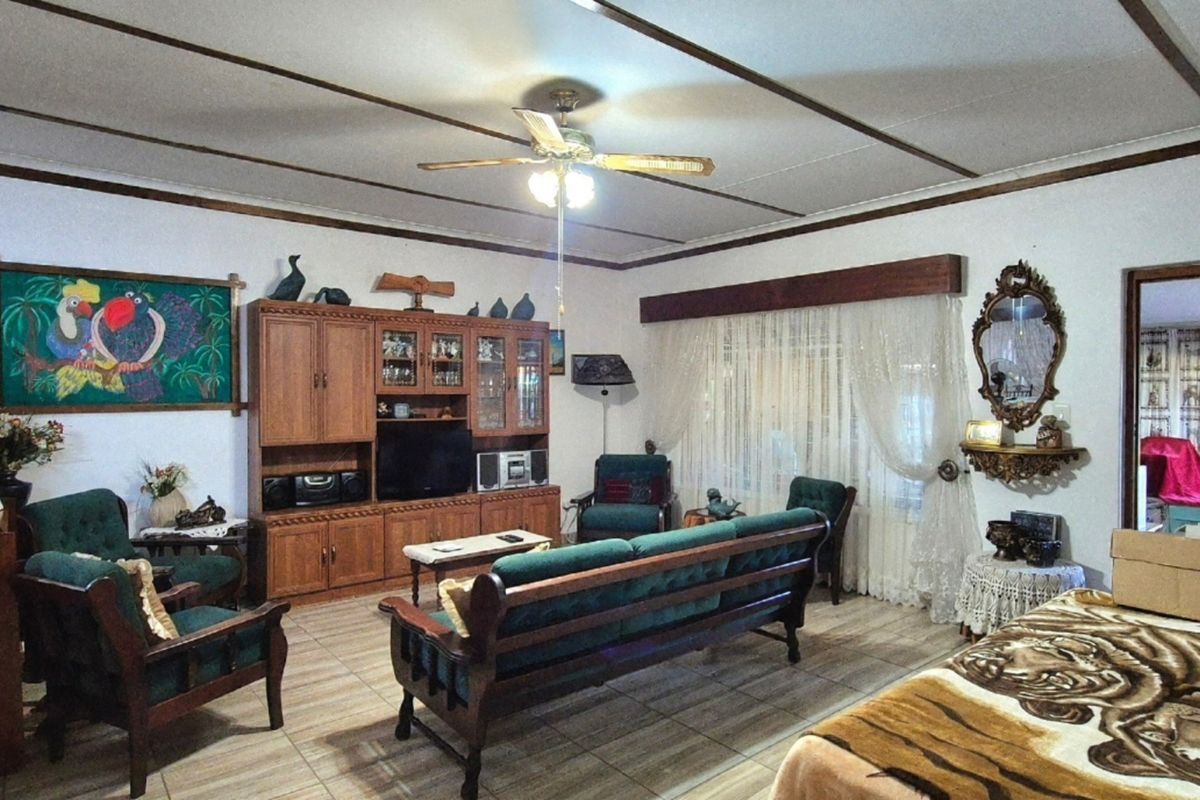 A spacious living room featuring tiled flooring, exposed ceiling beams, a central ceiling fan, and built-in wooden cabinetry.
