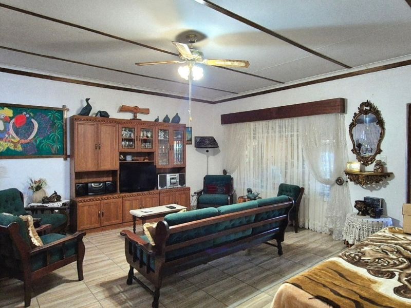 A spacious living room featuring tiled flooring, exposed ceiling beams, a central ceiling fan, and built-in wooden cabinetry.