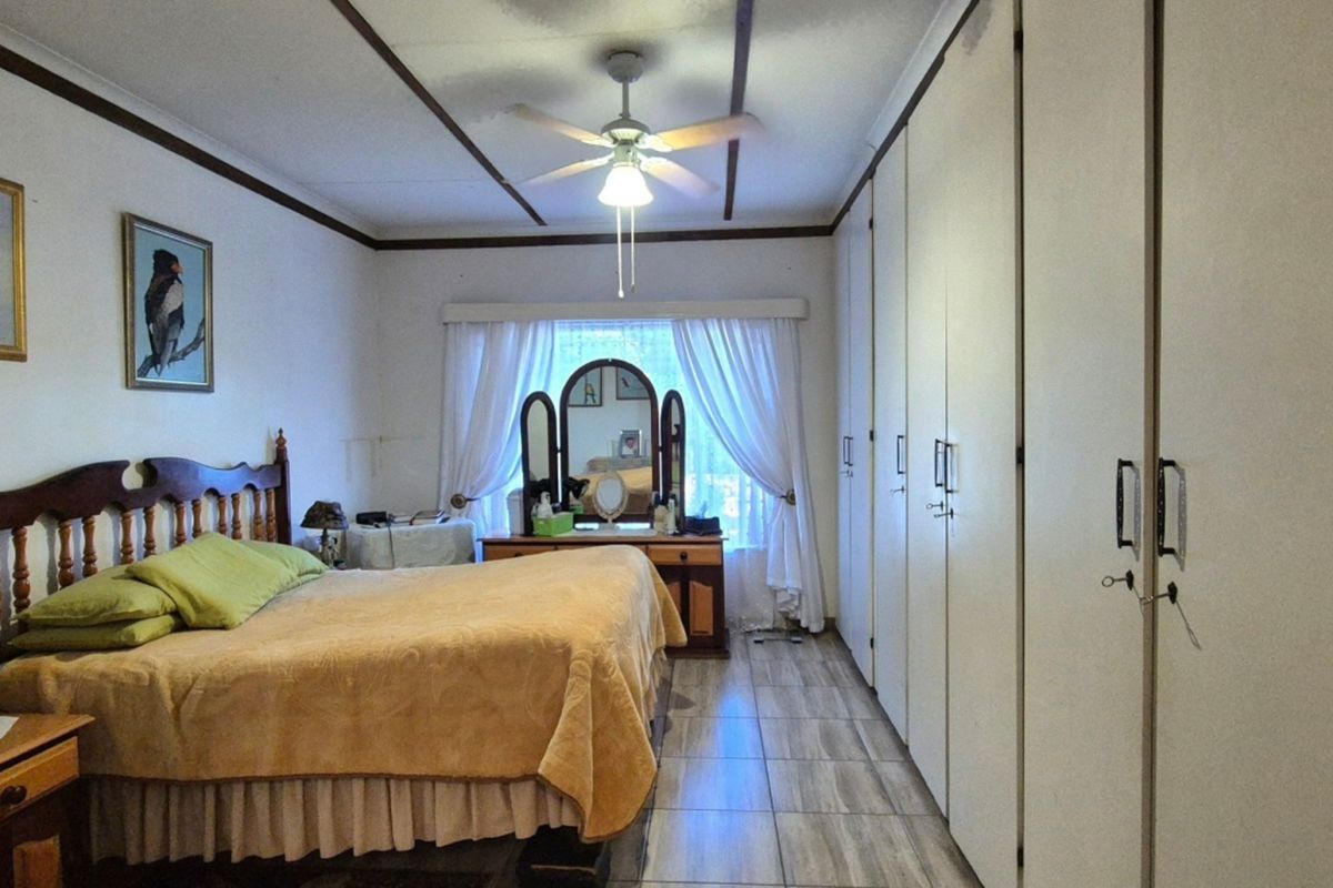 A spacious bedroom featuring extensive built-in cupboards, tiled flooring, and a ceiling fan, offering a functional and well-maintained living space.