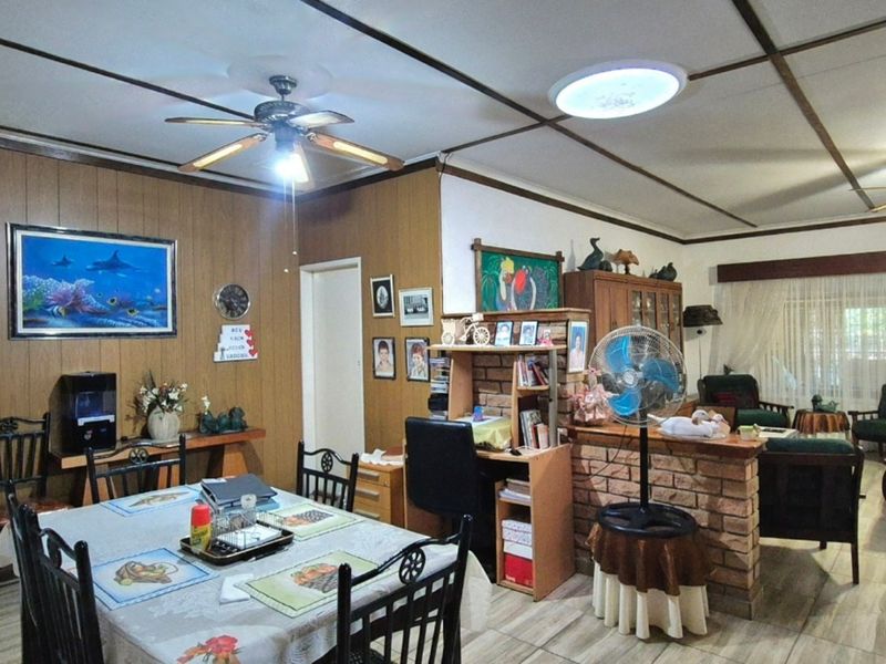 Open-plan living and dining area featuring tiled floors, exposed beam ceilings, and a brick partition wall, offering a functional layout with potential for modernization.