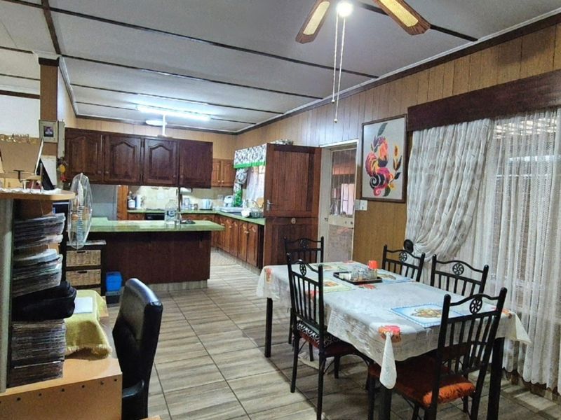 Open plan kitchen and dining area featuring wooden cabinetry, tiled flooring, and wood paneling, offering a dated aesthetic with potential for modernization.