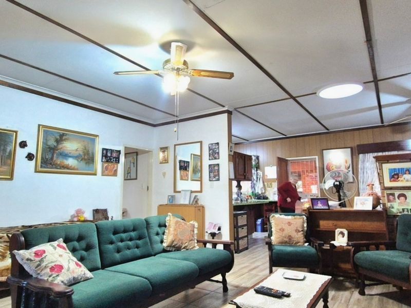 Open plan living area featuring exposed ceiling beams, ceiling fans, and tiled flooring, with an adjacent kitchen area visible in the background.
