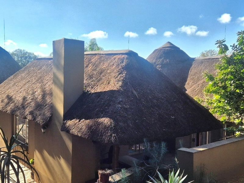Rear view of the property featuring traditional thatch roofing, a prominent chimney, and a paved outdoor patio area.