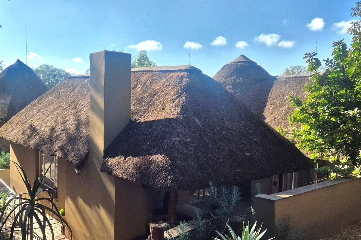 Rear view of the property featuring traditional thatch roofing, a prominent chimney, and a paved outdoor patio area.