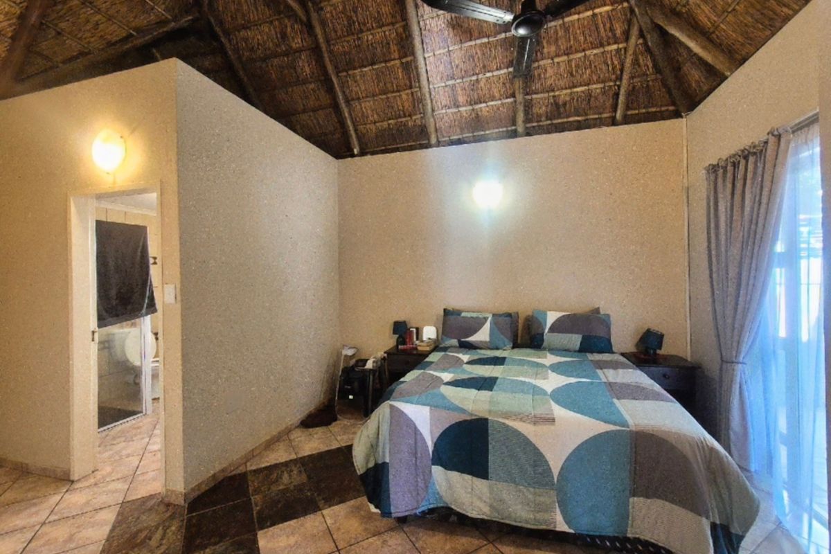 A bedroom featuring a high thatched ceiling, ceiling fan, tiled flooring, and an adjoining en-suite bathroom.