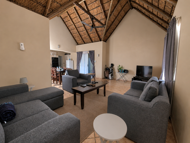 Spacious open-plan living area featuring a high vaulted thatched ceiling with exposed timber rafters, tiled flooring, and direct access to an outdoor space.