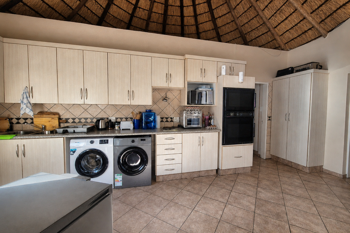 A functional kitchen featuring light wood cabinetry, a tiled backsplash, double wall oven, and a distinctive high-pitched thatch roof ceiling.