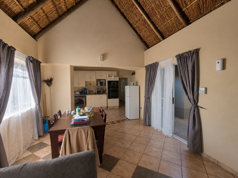 Open-plan living and dining area featuring a high vaulted thatched ceiling, tiled floors, and an integrated kitchen with built-in cabinetry and oven.