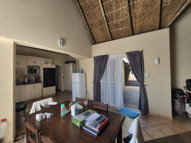 Open-plan living and kitchen area featuring a high thatched ceiling, tiled floors, and direct access to an outdoor patio through sliding glass doors.
