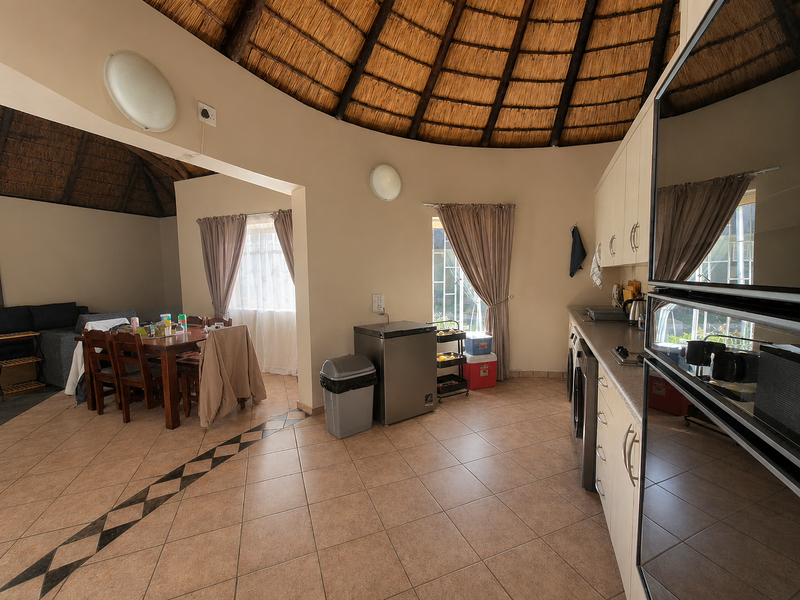 Open-plan living and kitchen area featuring a distinctive thatched roof, tiled flooring, and built-in cabinetry with integrated appliances.