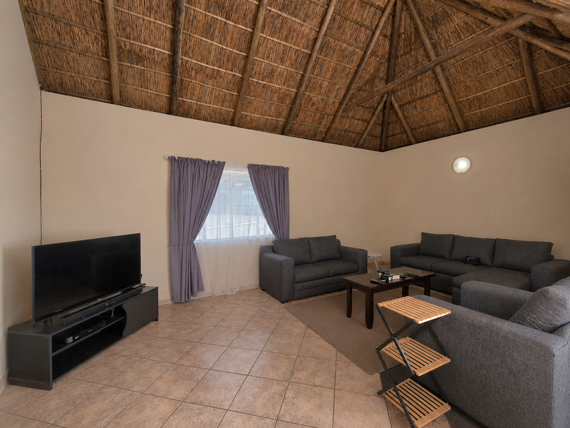 A spacious living room featuring a high vaulted thatched ceiling with exposed timber rafters and neutral tiled flooring.