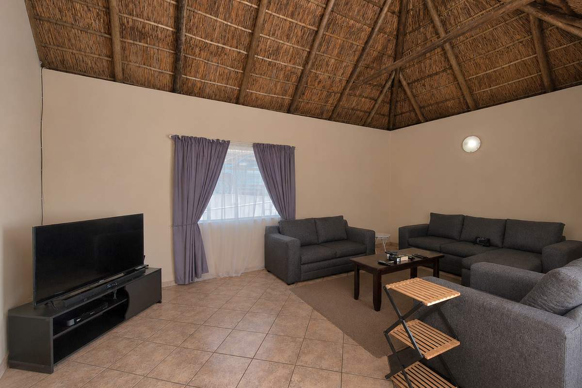 A spacious living room featuring a high vaulted thatched ceiling with exposed timber rafters and neutral tiled flooring.