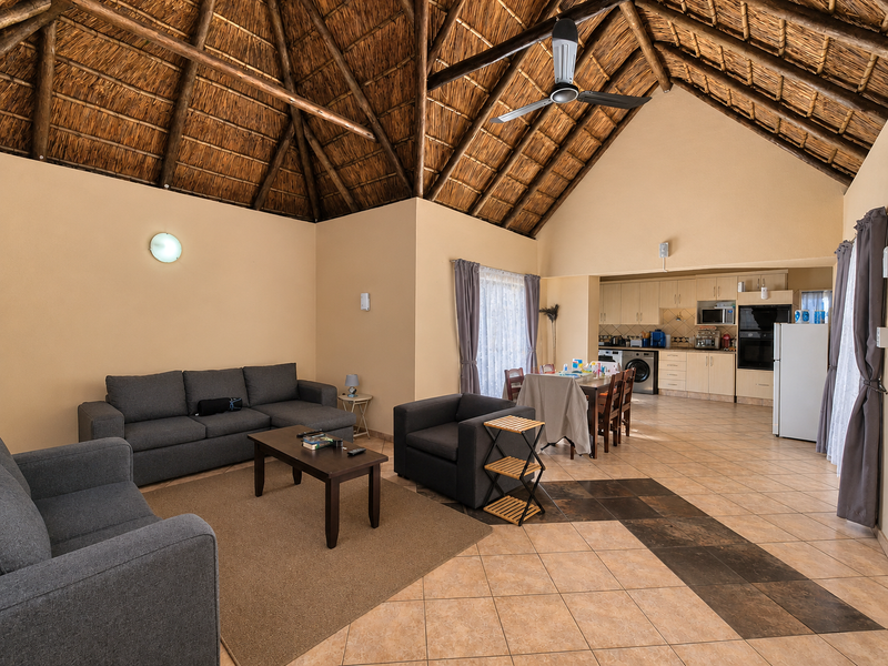 Spacious open-plan living and dining area featuring a high vaulted thatched ceiling with exposed timber rafters and a functional kitchen with built-in cabinetry.