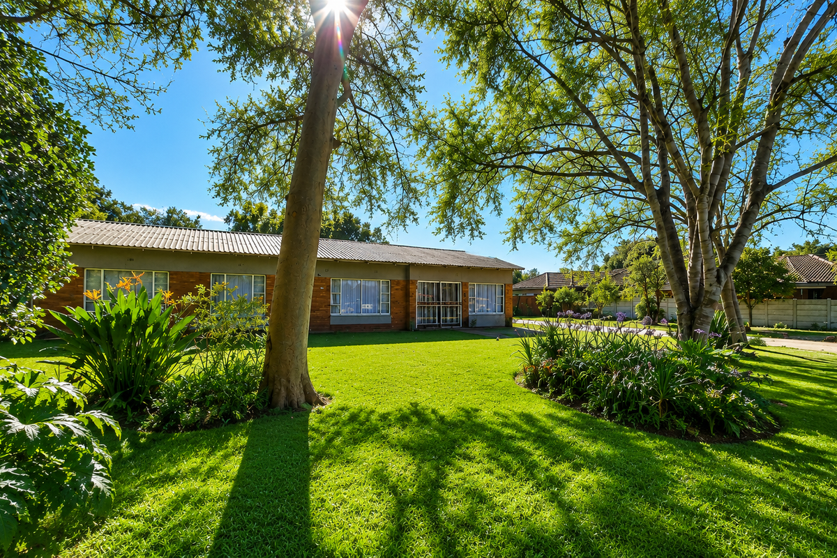 A spacious rear garden featuring a well-maintained lawn, mature trees, and a brick-built house with a tiled roof.