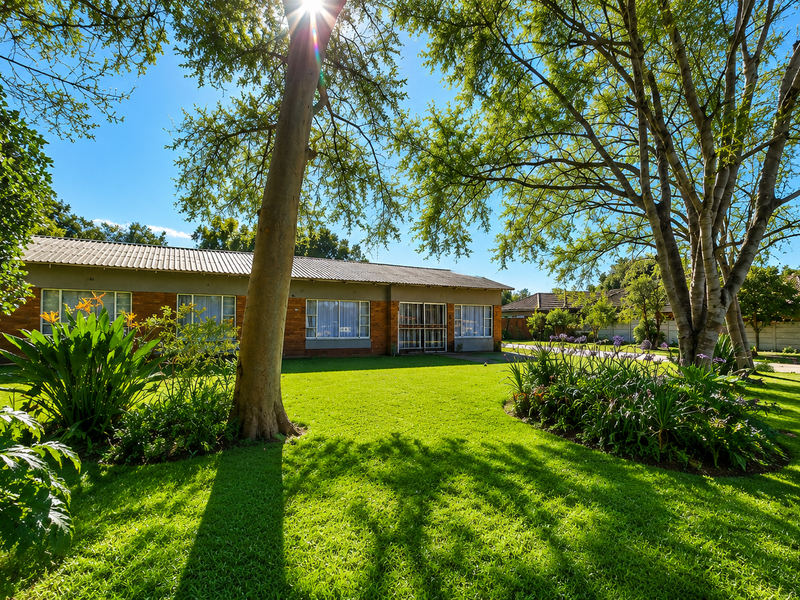 A spacious rear garden featuring a well-maintained lawn, mature trees, and a brick-built house with a tiled roof.