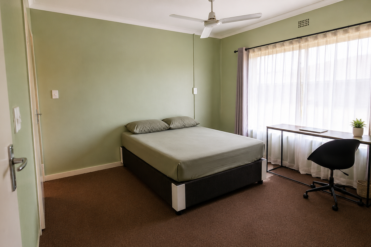 A well-lit bedroom featuring carpeted flooring, a ceiling fan, and large windows with curtain tracks, offering a comfortable and functional living space.
