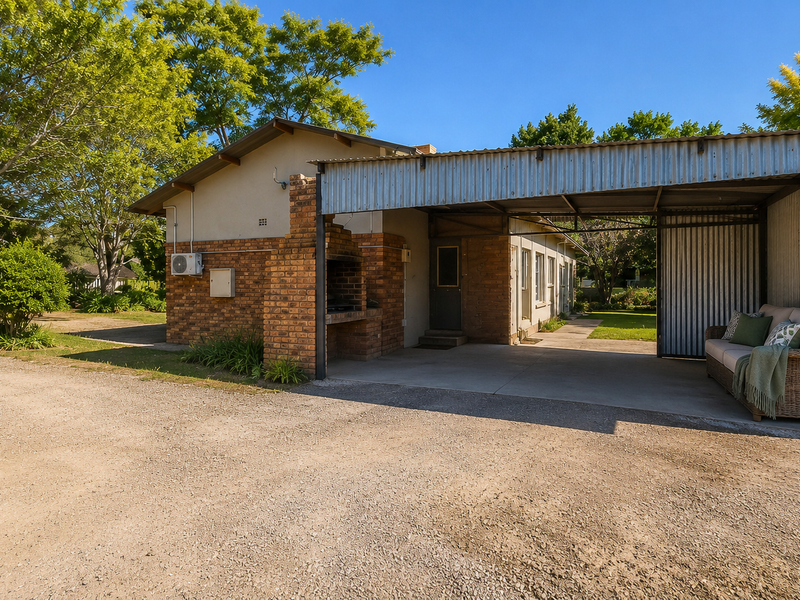 Rear exterior view featuring a covered patio area with a built-in brick braai, concrete flooring, and corrugated metal roofing structure.
