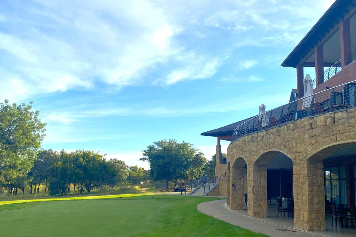 A view of the rear elevation featuring stone masonry arches, a covered patio area, and a balcony overlooking the landscaped golf course grounds.