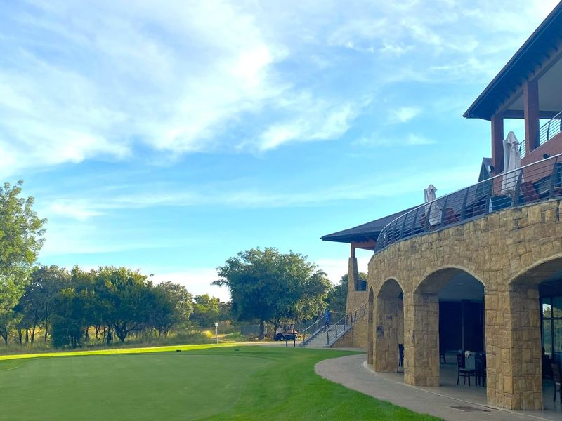 A view of the rear elevation featuring stone masonry arches, a covered patio area, and a balcony overlooking the landscaped golf course grounds.
