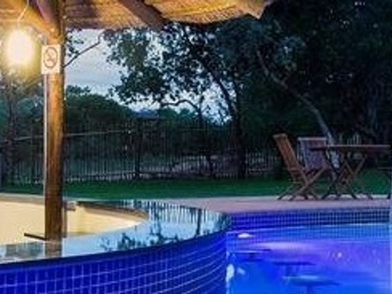 A well-maintained swimming pool area featuring a thatched gazebo, blue mosaic tiling, and a metal perimeter fence, perfect for outdoor relaxation.