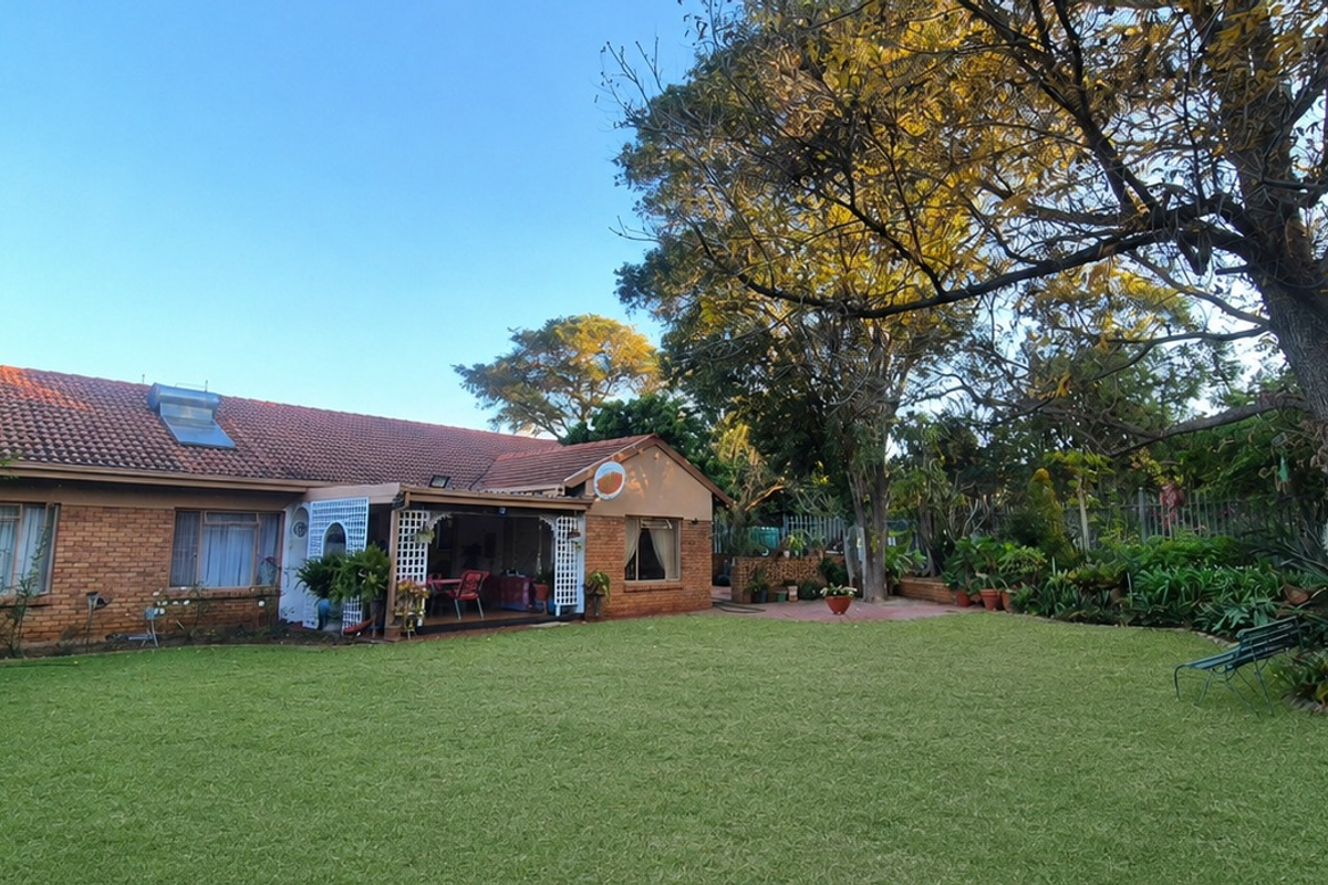 Rear view of a brick house featuring a well-maintained lawn, mature trees, and a covered patio area.
