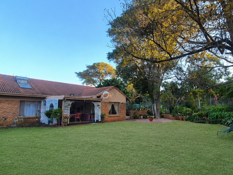 Rear view of a brick house featuring a well-maintained lawn, mature trees, and a covered patio area.