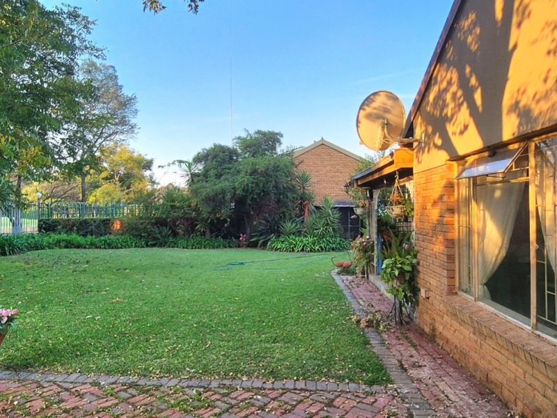A spacious rear garden featuring a well-maintained lawn, brick paving, and a brick-clad exterior wall with a satellite dish.