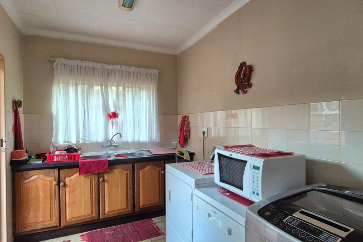 A functional kitchen featuring wooden cabinetry, a double basin sink, and tiled splashbacks, offering a practical layout with space for laundry appliances.
