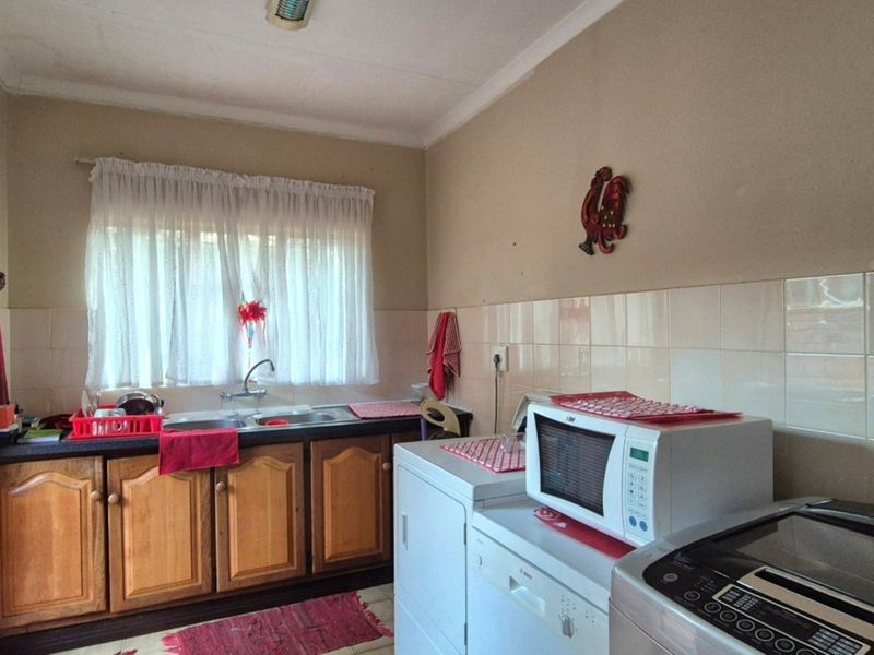 A functional kitchen featuring wooden cabinetry, a double basin sink, and tiled splashbacks, offering a practical layout with space for laundry appliances.