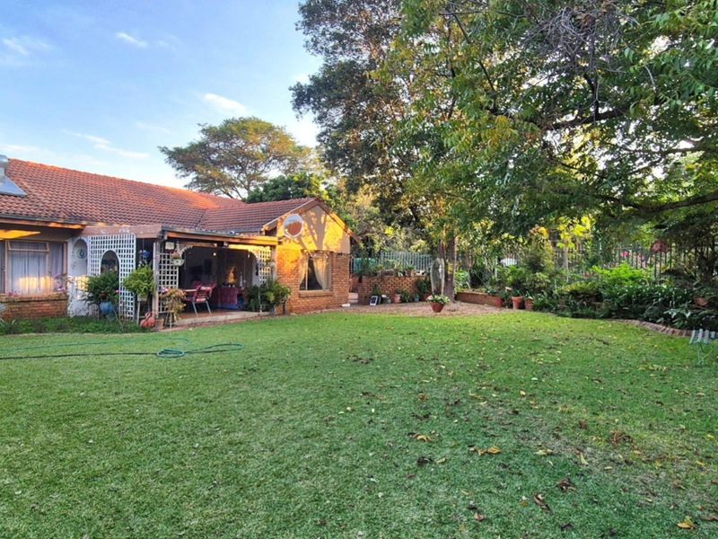 A view of the rear of the house featuring a brick facade, tiled roof with solar geyser, and a covered patio overlooking a spacious garden.