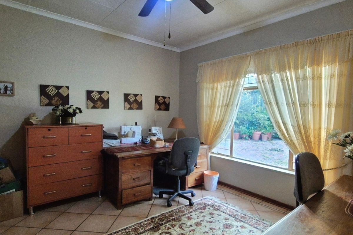A functional bedroom featuring tiled flooring, a ceiling fan, and a large window providing natural light and garden views.