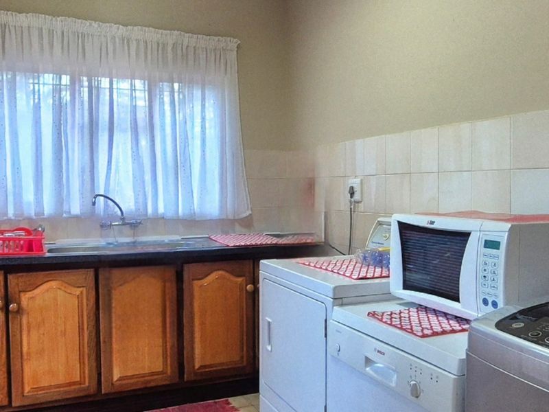 Functional laundry room featuring built-in wooden cabinetry, a stainless steel sink, tiled backsplash, and dedicated space for multiple appliances.