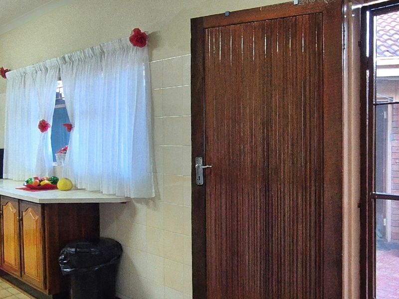 A functional kitchen area featuring wooden cabinetry, tiled wall finishes, and direct access to an outdoor area through a secure wooden door.