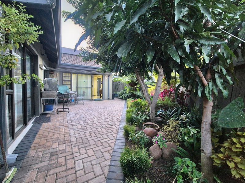 A well-maintained brick-paved patio area featuring mature garden landscaping and direct access to the home through sliding glass doors.