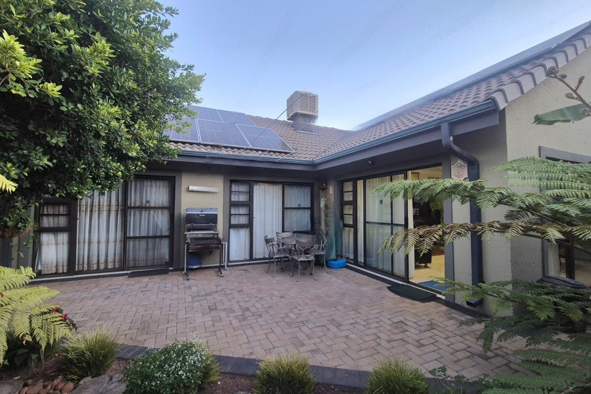 Rear exterior view featuring a paved patio area, sliding glass doors, solar panels, and an evaporative cooling unit on the tiled roof.