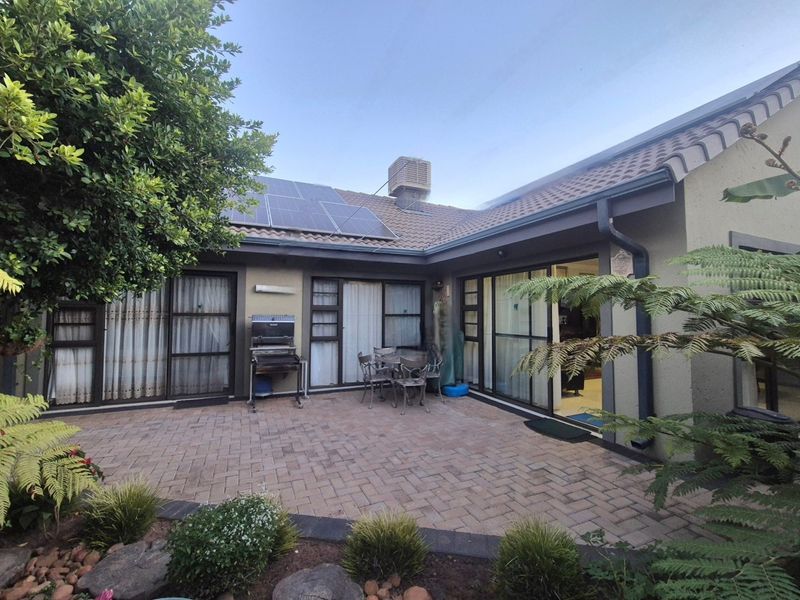Rear exterior view featuring a paved patio area, sliding glass doors, solar panels, and an evaporative cooling unit on the tiled roof.