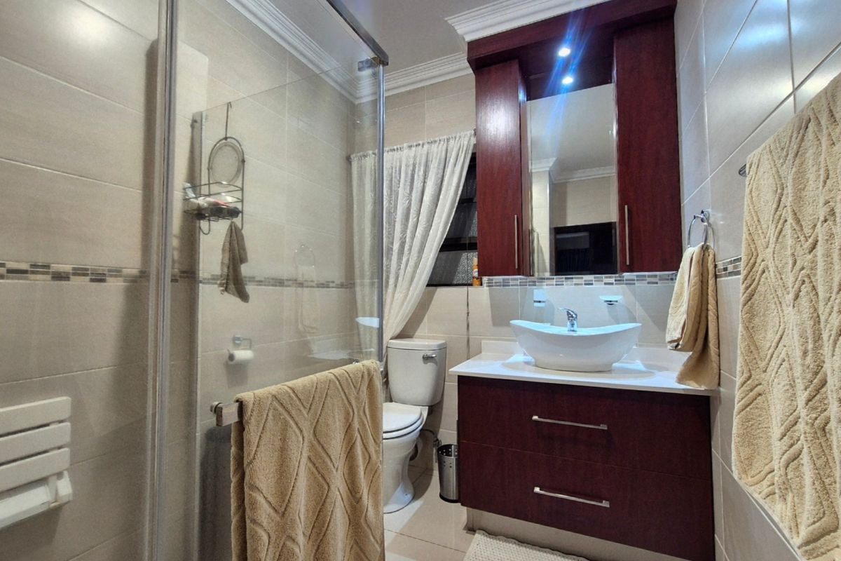 A well-maintained bathroom featuring a glass shower enclosure, a modern vessel sink with a dark wood vanity, and neutral wall tiling.