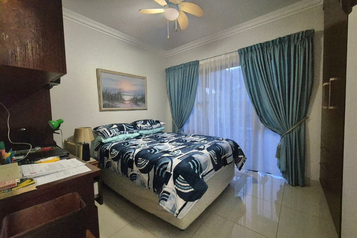 A well-maintained bedroom featuring tiled flooring, a ceiling fan, crown molding, and a built-in wardrobe with access to a patio through sliding glass doors.