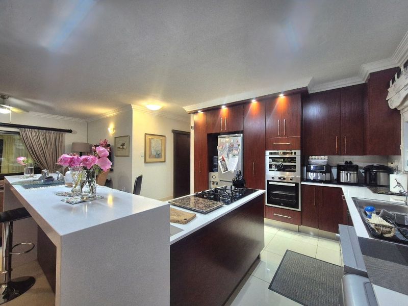 Modern kitchen featuring dark wood cabinetry, a large stone-topped island with integrated gas hob, built-in oven, and sleek tiled flooring.