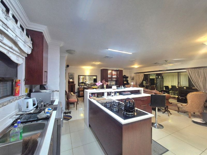 Spacious open-plan kitchen and living area featuring a central island with gas cooktop, tiled flooring, and large sliding doors leading to the outdoor space.