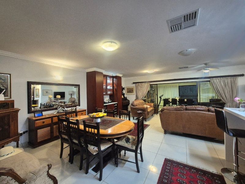 Spacious open-plan living and dining area featuring tiled floors, a built-in bar, and large sliding doors leading to an outdoor patio space.
