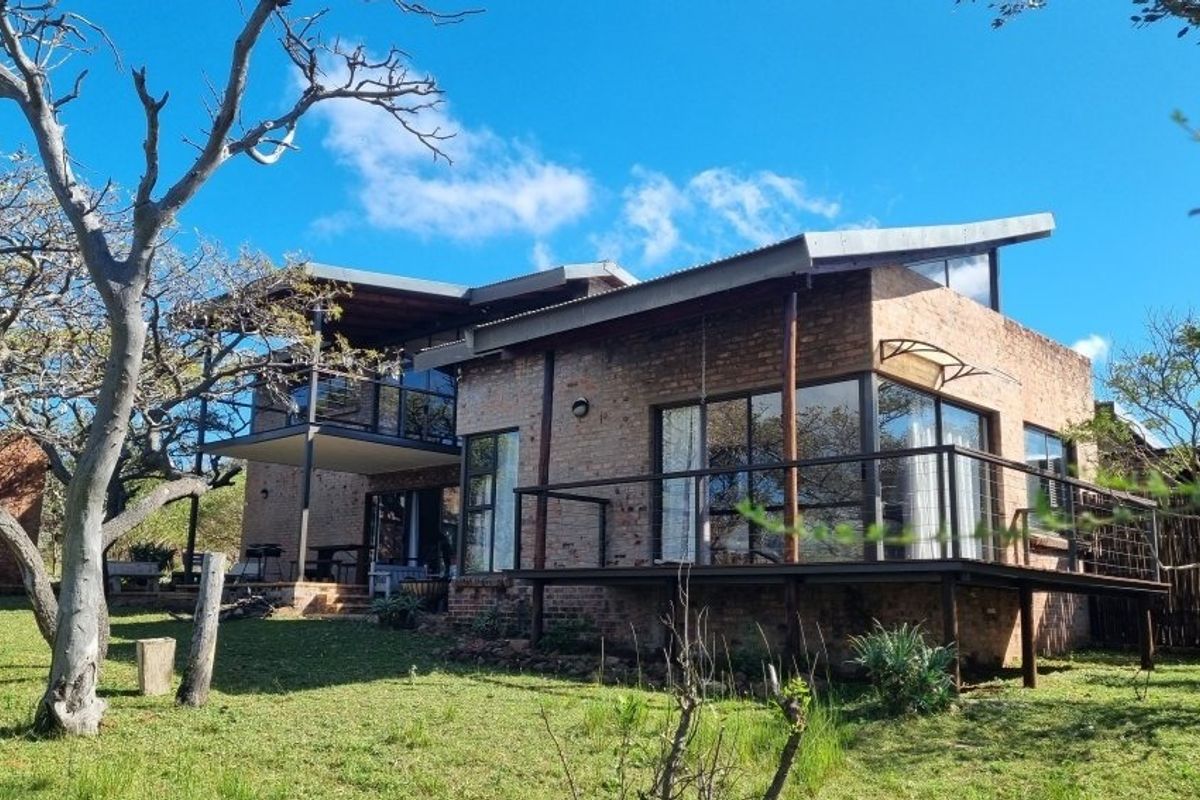 A modern double-story home featuring exposed brickwork, a raised timber deck, and large glass sliding doors overlooking a spacious garden.