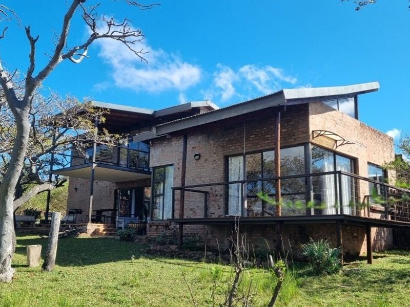 A modern double-story home featuring exposed brickwork, a raised timber deck, and large glass sliding doors overlooking a spacious garden.