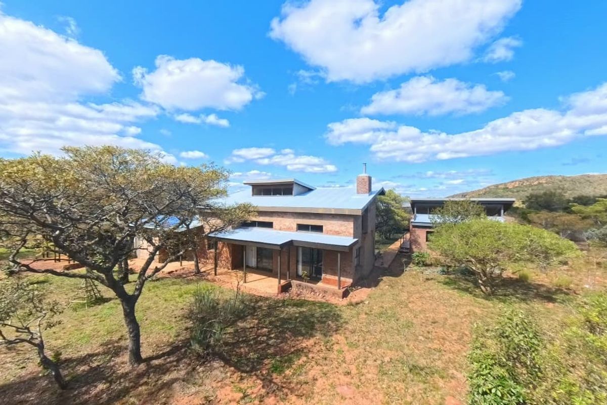 Aerial view of a rustic, exposed brick house featuring a metal roof, brick chimney, and covered patio set within a natural landscape.