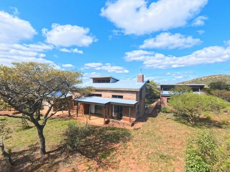 Aerial view of a rustic, exposed brick house featuring a metal roof, brick chimney, and covered patio set within a natural landscape.