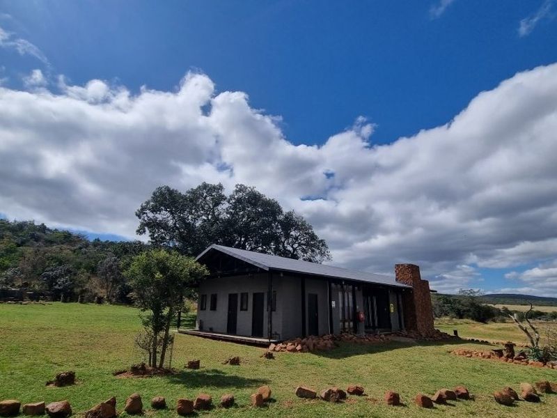 A detached single-story dwelling featuring a stone chimney, metal roof, and timber decking, set within a spacious rural landscape.