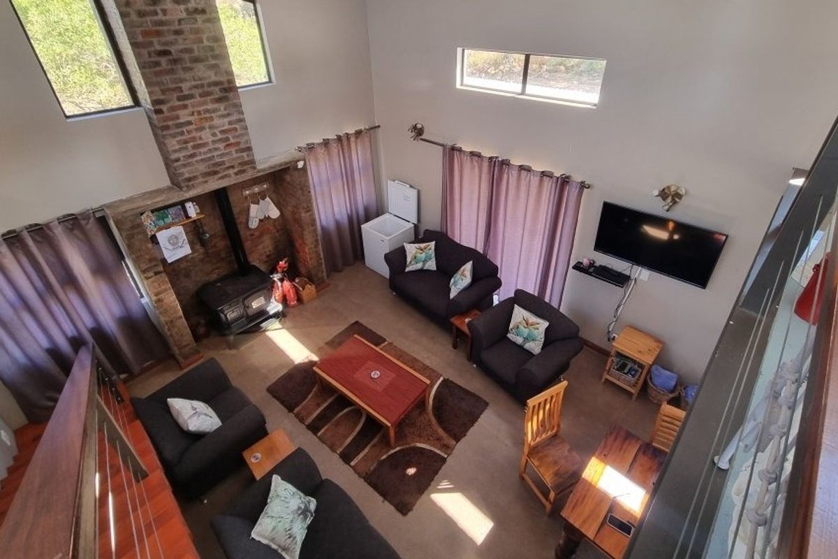 Spacious double-volume living area featuring an exposed brick fireplace with a wood-burning stove and large windows providing ample natural light.