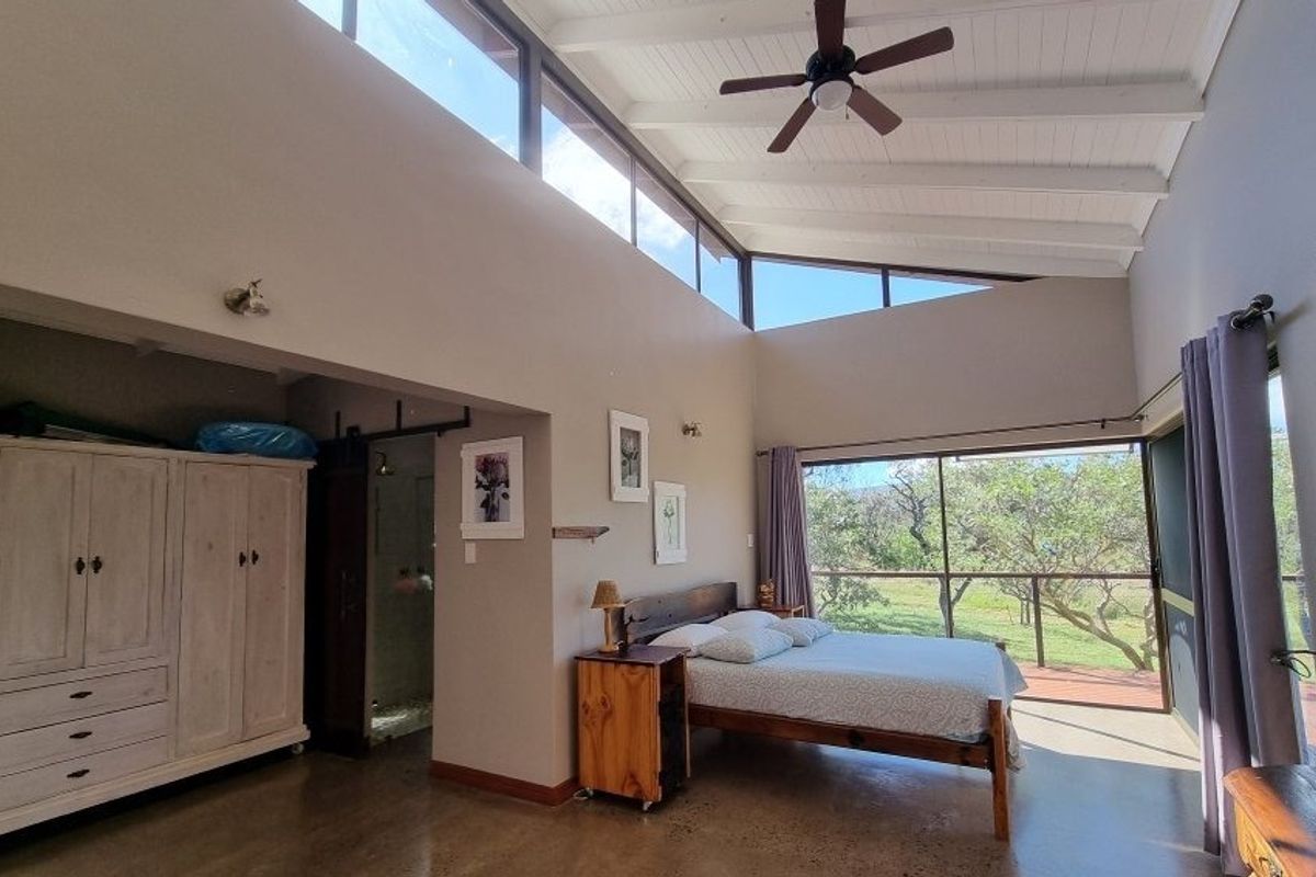 Spacious bedroom featuring high vaulted ceilings with exposed rafters, polished concrete floors, and large clerestory windows providing abundant natural light and garden views.